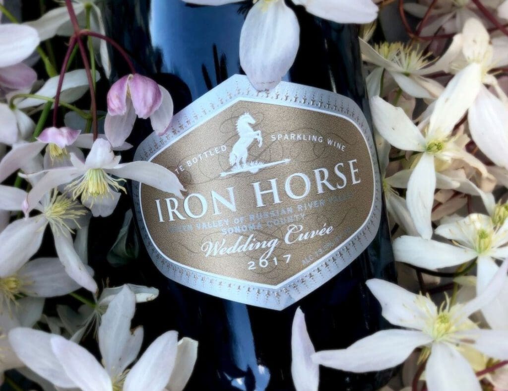 A bottle of Iron Horse Wedding Cuvée sparkling wine surrounded by white flowers.