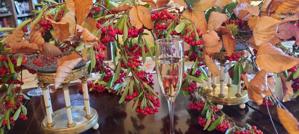A glass of champagne surrounded by autumn leaves and red berries on a festive table.