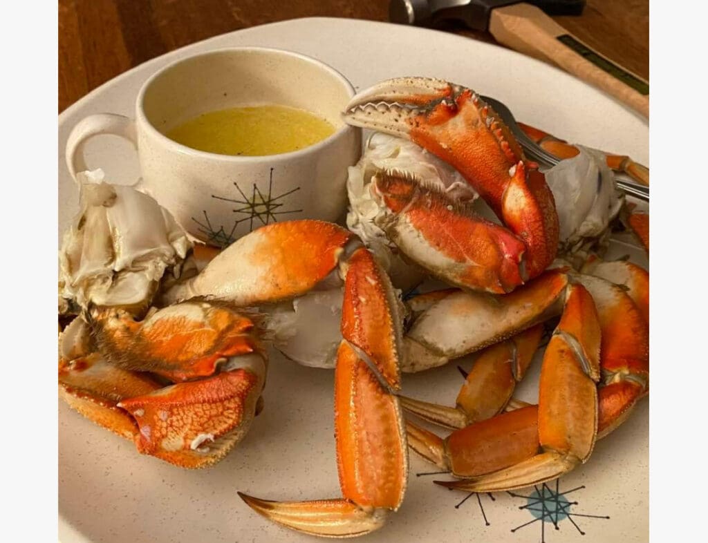 Plate of cooked crab legs with a cup of melted butter for dipping on a white dish.