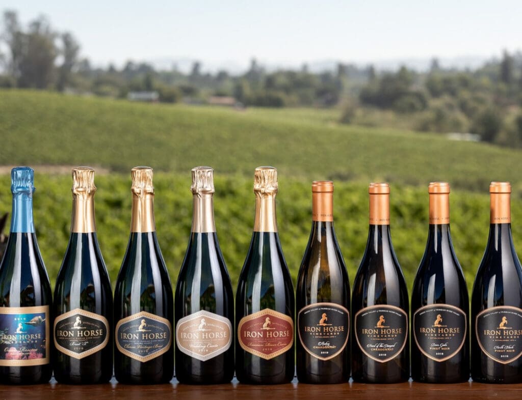 Nine bottles of Iron Horse wine on a table with a vineyard landscape in the background.