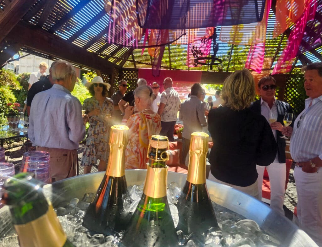 People socializing at an outdoor party with champagne bottles chilling in ice in the foreground.