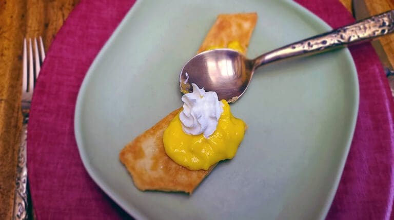 A dessert with a pastry, yellow custard, and whipped cream on a plate with a spoon.