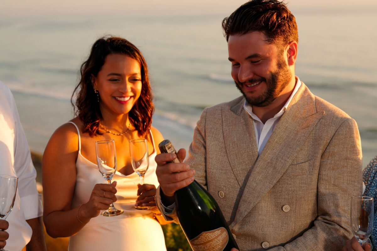 a couple at a coastal wedding opening a magnum of wedding cuvee