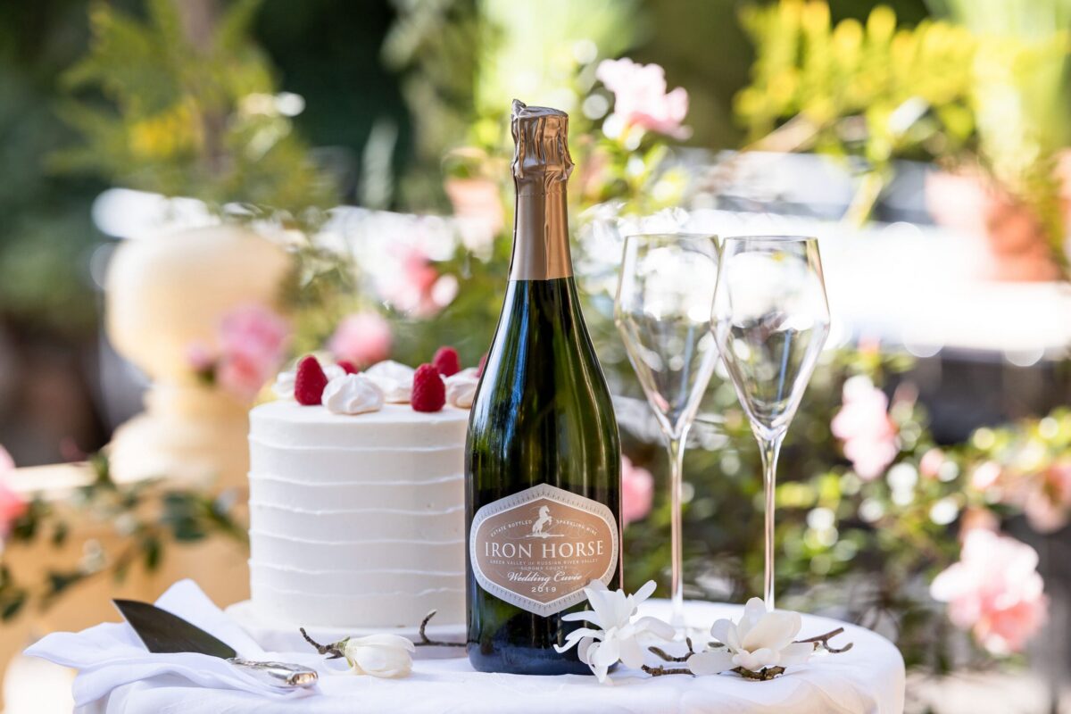 a bottle of wedding cuvee on a table with a white cake and two flutes