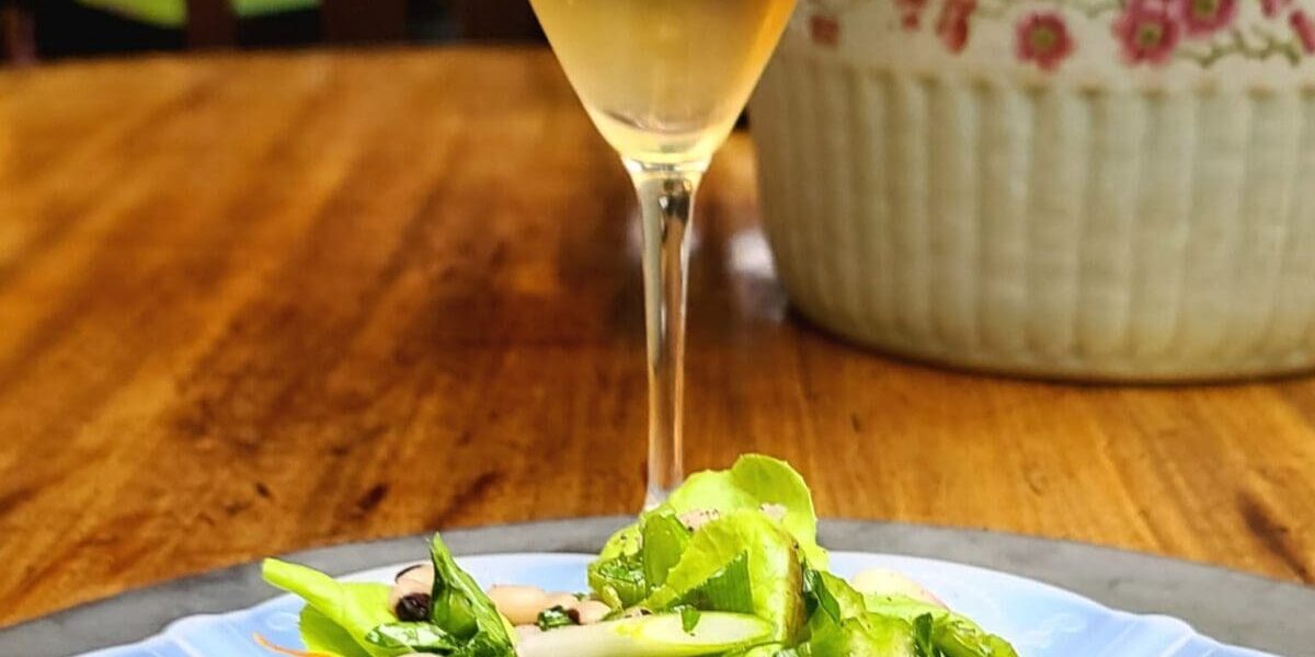 A fresh salad with greens and radishes on a plate, next to a glass of sparkling wine on a wooden table.