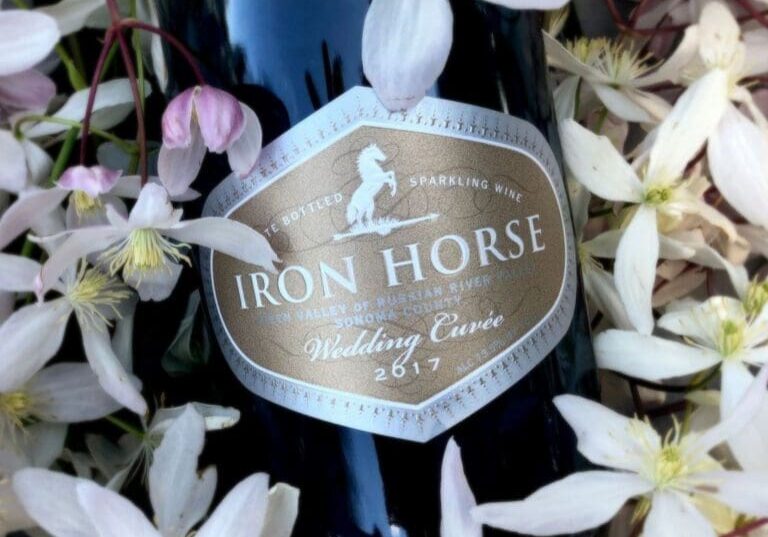 A bottle of Iron Horse Wedding Cuvée sparkling wine surrounded by white flowers.
