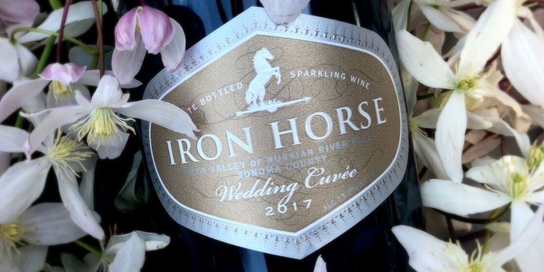 2017-Wedding-Cuvee-web A bottle of Iron Horse Wedding Cuvée sparkling wine surrounded by white flowers.