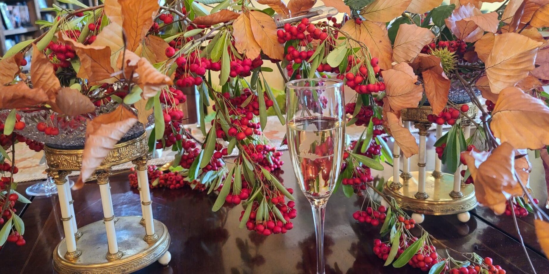 A glass of champagne surrounded by autumn leaves and red berries on a festive table.