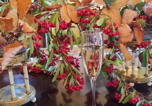 A glass of champagne surrounded by autumn leaves and red berries on a festive table.