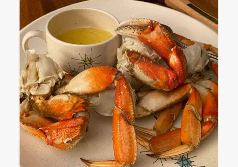 Plate of cooked crab legs with a cup of melted butter for dipping on a white dish.