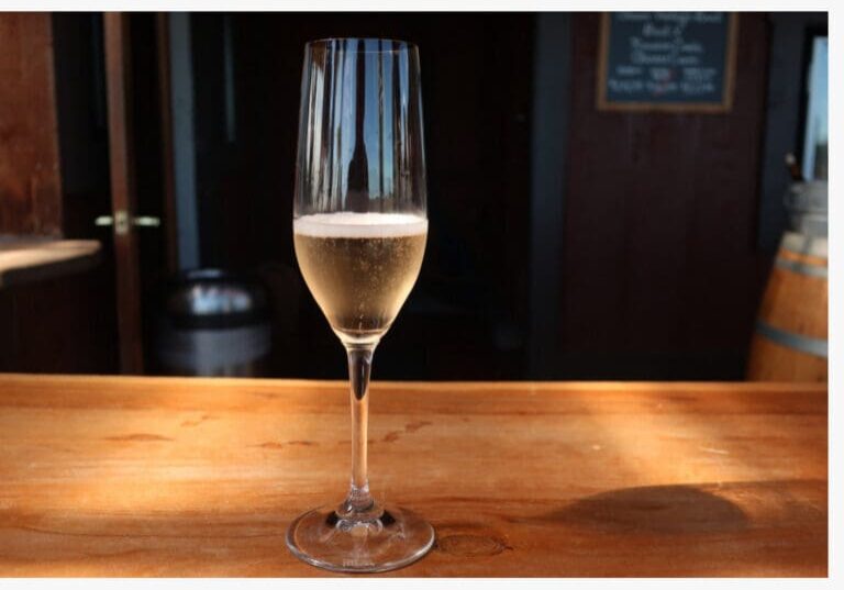 A glass of sparkling wine on a wooden bar with a dark background and light shining on the glass.