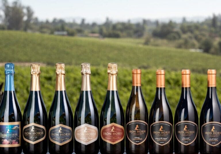 Nine bottles of Iron Horse wine on a table with a vineyard landscape in the background.