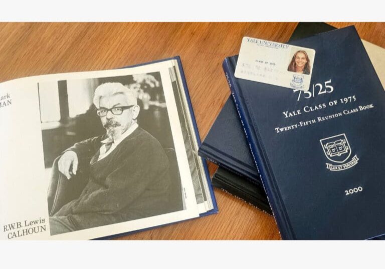 Open book with a black-and-white portrait, Yale reunion books, and an ID card on a wooden table.