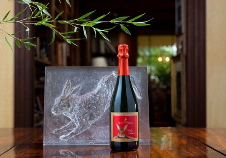 A bottle of Iron Horse sparkling wine with a red label sits next to a rabbit sculpture on a wooden table.