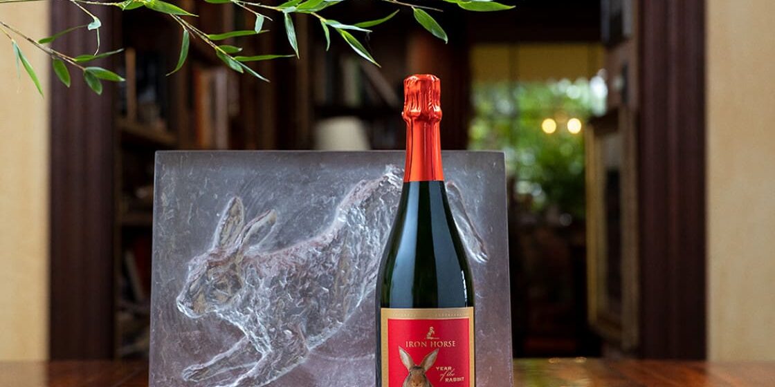 A bottle of Iron Horse sparkling wine with a red label sits next to a rabbit sculpture on a wooden table.