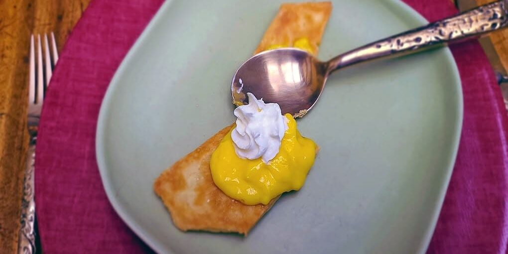 A dessert with a pastry, yellow custard, and whipped cream on a plate with a spoon.