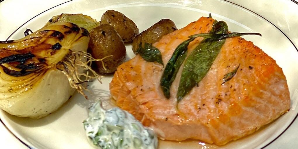 Salmon fillet with herbs, roasted potatoes, grilled fennel, and a dollop of creamy herb sauce on a plate.