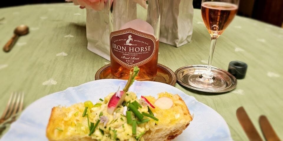 A plate with toast and salad, next to a bottle and glass of rosé wine, with pink flowers in the background.