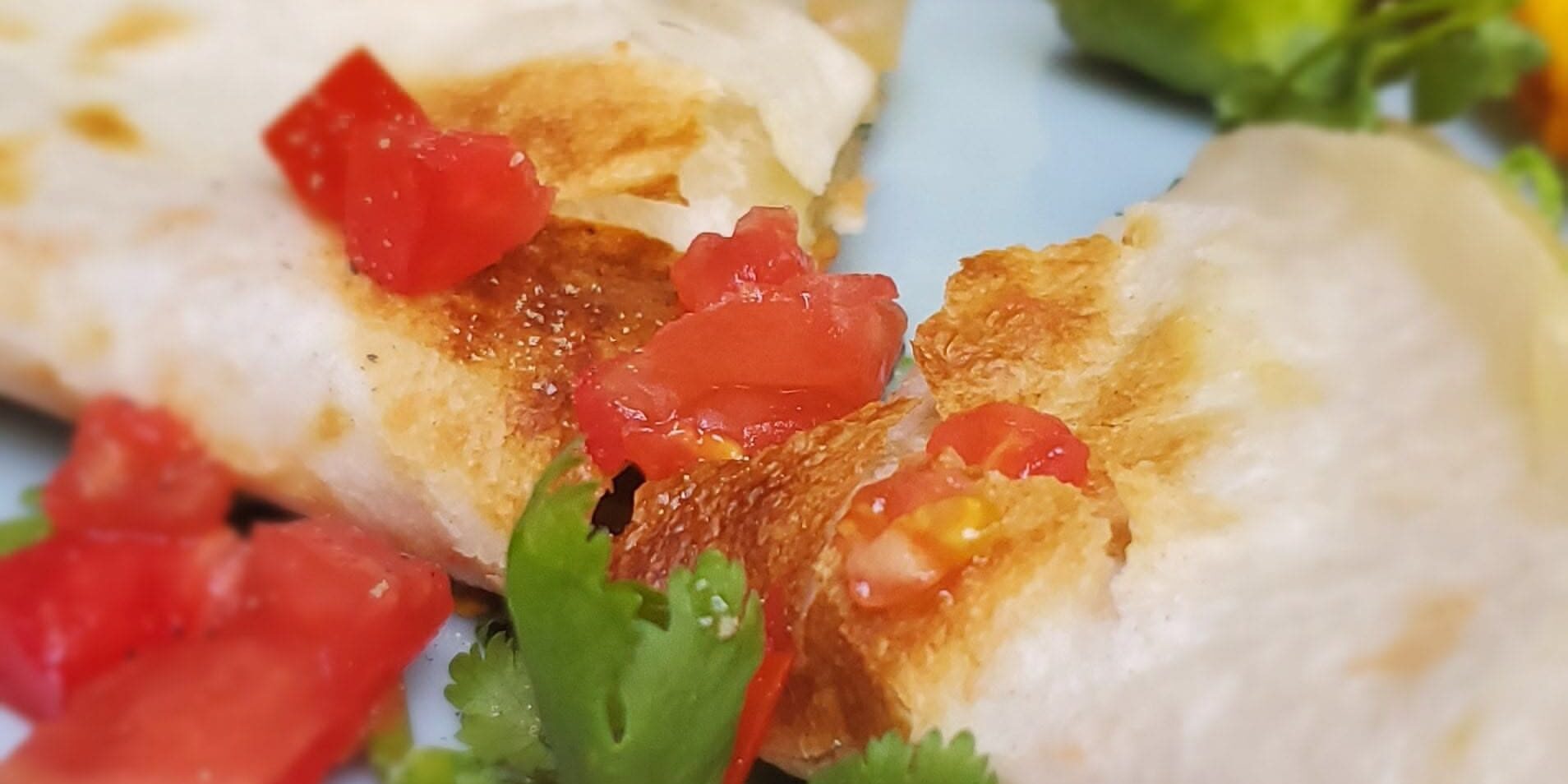 Squash-Blossom-Quesadilla-2 A close-up of a quesadilla topped with diced tomatoes and fresh cilantro on a plate.