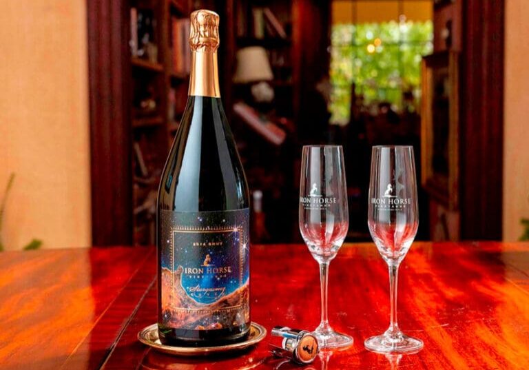 A bottle of Iron Horse sparkling wine and two empty glasses sit on a polished wooden table.