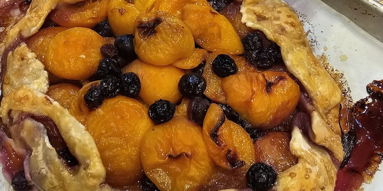 Rustic fruit galette with golden apricots and dark berries on a baking sheet, crust edges folded over.