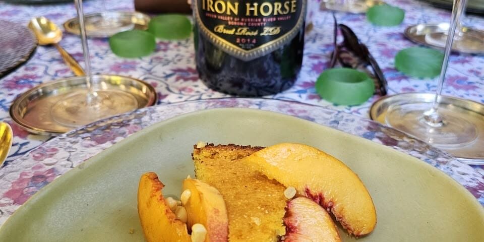 corn-pie-and-peaches-scaled A dessert with peach slices and corn on a plate, with Iron Horse wine and glasses on a floral table setting.