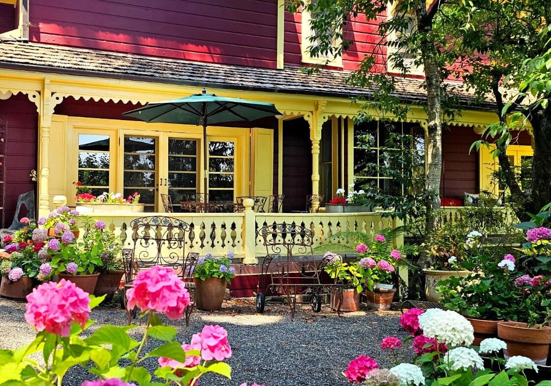 A colorful garden with blooming hydrangeas in front of a red and yellow house with a shaded patio.