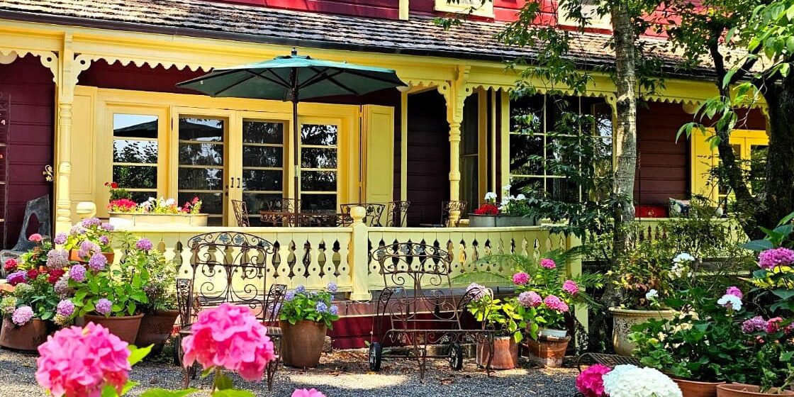 A colorful garden with blooming hydrangeas in front of a red and yellow house with a shaded patio.