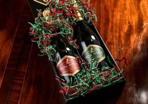 Two bottles of Iron Horse sparkling wine in a gift box with red and green decorative paper on a wood table.