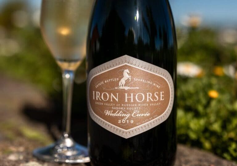 A bottle of Iron Horse sparkling wine beside a filled glass, outdoors with blurred greenery and flowers.