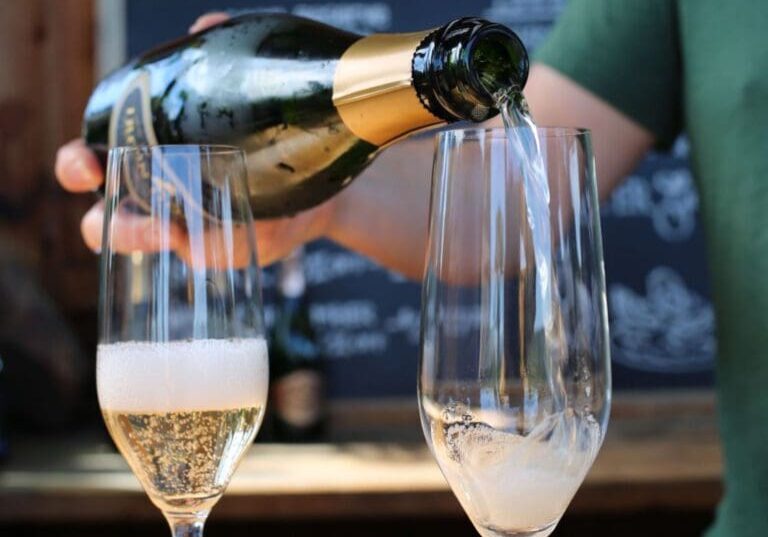 A person pours sparkling wine into a glass beside another glass partially filled with bubbles.