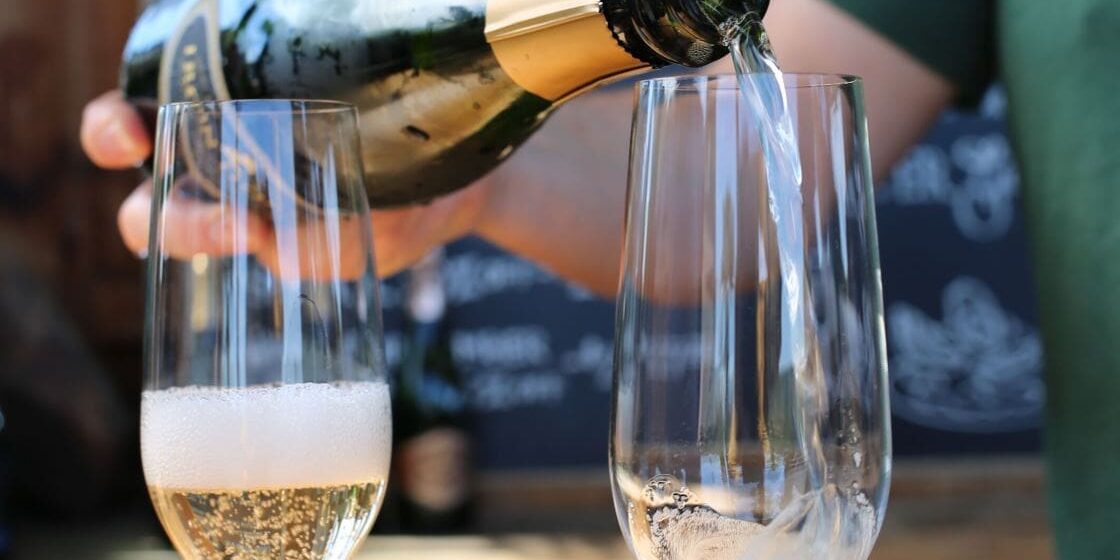 pouring-sparkling-wine A person pours sparkling wine into a glass beside another glass partially filled with bubbles.