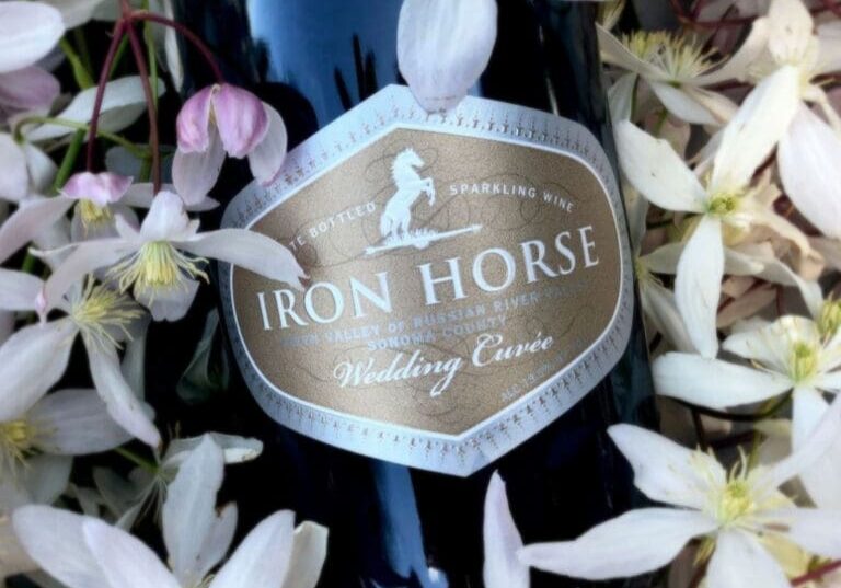 Iron Horse sparkling wine bottle labeled “Wedding Cuvée” surrounded by pale pink and white flowers.