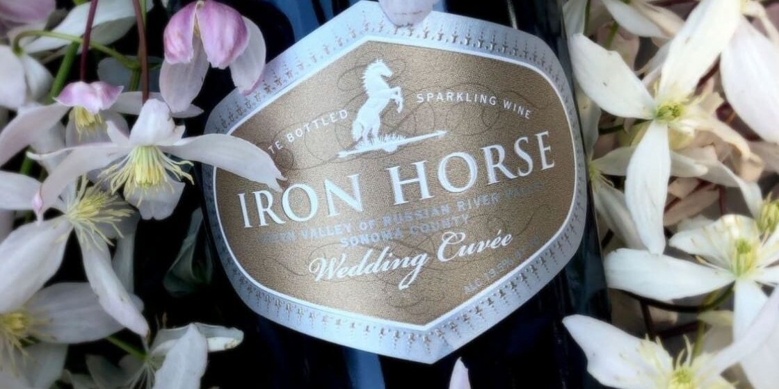 Iron Horse sparkling wine bottle labeled “Wedding Cuvée” surrounded by pale pink and white flowers.